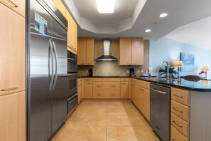 A modern kitchen with stainless steel appliances, wooden cabinets, and a tiled floor.