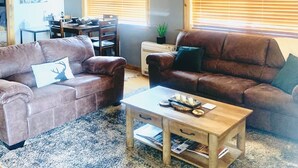 Een gezellige woonkamer met twee bruine leren banken, een houten salontafel en een eethoek met tafel en stoelen.