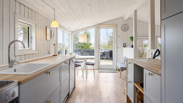 A kitchen with wooden cabinets, a sink, and a dining area with a table and chairs. - 3 bedroom awesome home in Glesborg (Glesborg)