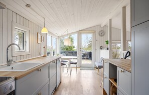 A kitchen with wooden cabinets, a sink, and a dining area with a table and chairs. - 3 bedroom awesome home in Glesborg (Glesborg)