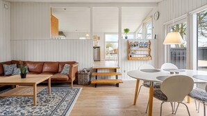A modern interior with a brown leather sofa, a wooden coffee table, a white dining table with chairs, and a bookshelf. - 3 bedroom awesome home in Glesborg (Glesborg)