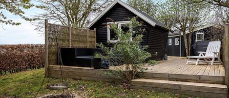 Uma cabana de madeira com um alpendre, um espaço de estar ao ar livre e um jardim com uma árvore e plantas.