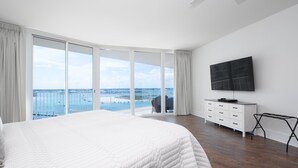 Un dormitorio con una cama grande, televisor, cómoda y balcón con vista al mar.