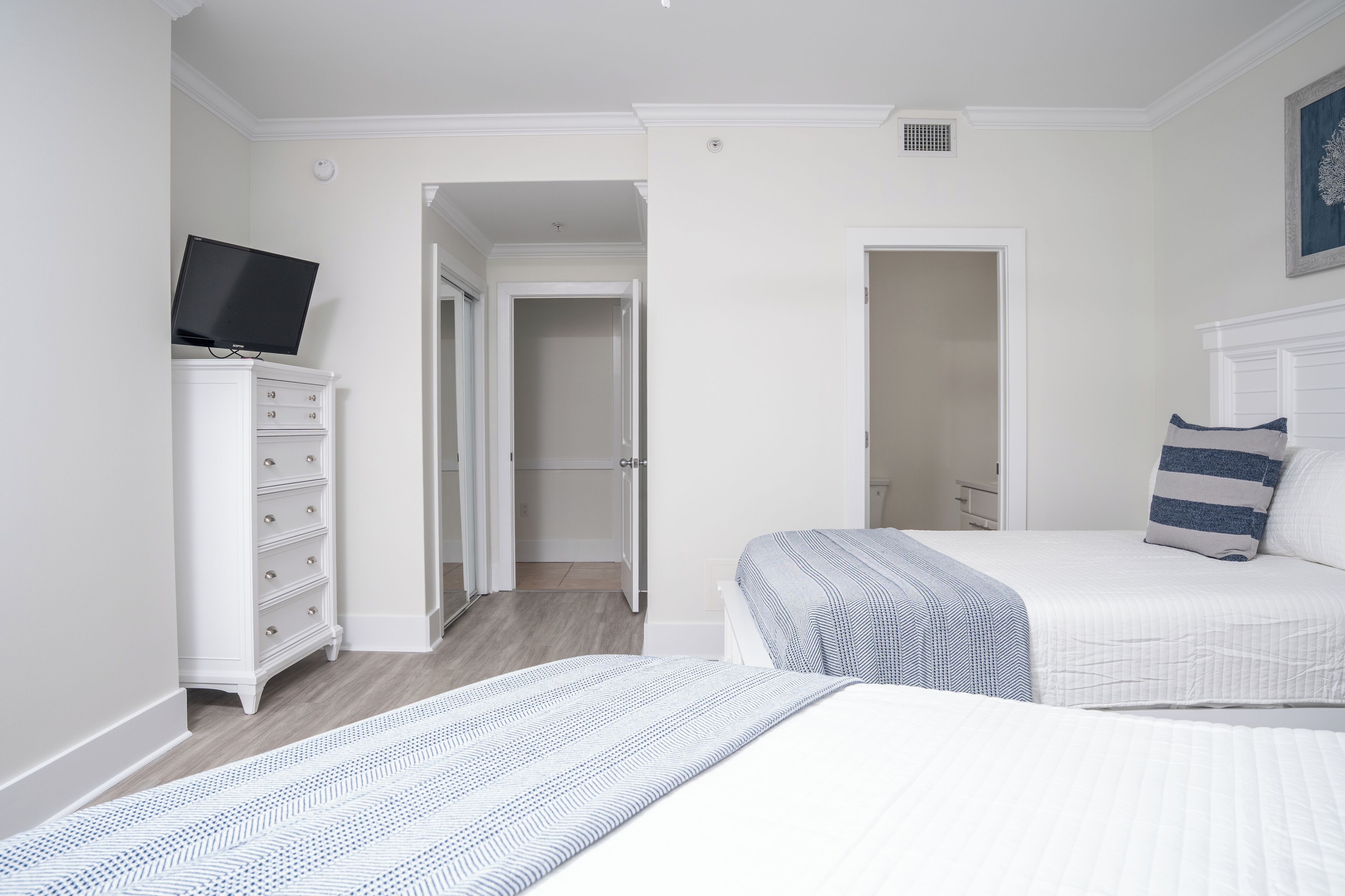 A bedroom with two beds, a TV on a dresser, and a hallway leading to another room.