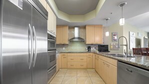 A kitchen with stainless steel appliances, wooden cabinets, a tiled floor, and a modern pendant light. - Condo with Panoramic Views of Gulf of Mexico. Complimentary Boat Slip! (Orange Beach)