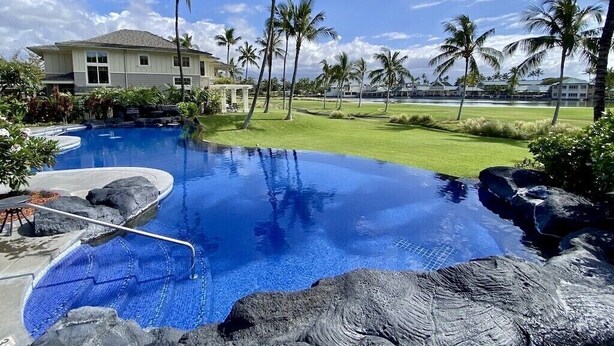 A resort with a swimming pool, palm trees, and a house in the background. - Island Therapy - Walk to A-Bay, Shops & Dining - Golf Views - Sleeps 6 (Waikoloa)