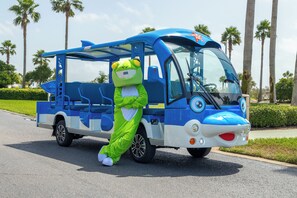 A mascot in a green frog costume standing next to a blue and white bus. - Experience Boat Life from this Luxurious Three Bedroom Unit. Complimentary Boat Slip! (Orange Beach)