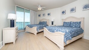 A bedroom with two beds, a ceiling fan, and a view of the sea through a large window. - Beautiful Family-Friendly Corner Condo with Panoramic Views! Complimentary Boat Slip! (Orange Beach)