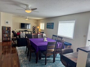 A dining area with a purple tablecloth, wooden chairs, a ceiling fan, a bookshelf, a TV, and a window with blinds. - Canyon House near Yellowstone  (Gardiner)