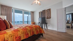 A bedroom with a large bed, a ceiling fan, a TV, and a view of the sky through the window.