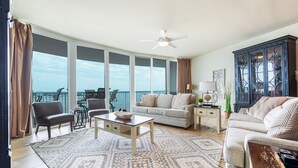 A spacious living room with a large window, a ceiling fan, a sofa, a coffee table, and a cabinet.