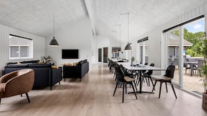 A spacious living area with a large TV, dark sofas, and a dining table with chairs. - Nice home in Sydals with sauna (Sydals)