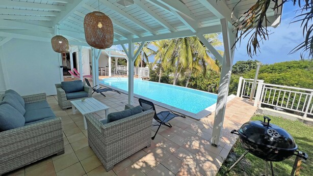 A covered outdoor area with a pool, wicker furniture, and a grill. - Beautiful villa with sea view and infinity pool (Saint François)