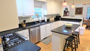 A modern kitchen with white cabinets, a black countertop, stainless steel appliances, and a central island with stools. - Winter in the mountains, fishing by the fire pit. Murphy and the Casino nearby. (Murphy)