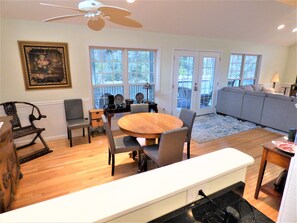 A spacious living room with a dining area, large windows, and a ceiling fan.
