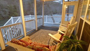 A covered porch with wicker furniture, a potted plant, and a view of a dock and trees. - Winter in the mountains, fishing by the fire pit. Murphy and the Casino nearby. (Murphy)