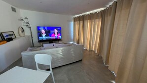 A living room with a TV, a sofa, a chair, and curtains.