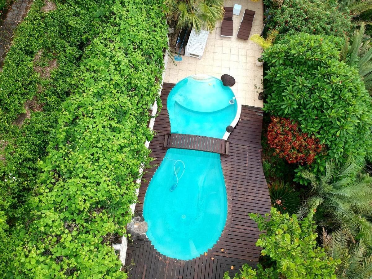 Ein rechteckiger Pool mit Holzterrasse, umgeben von üppiger Bepflanzung und einer kleinen Sitzecke mit Liegestühlen.