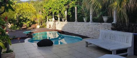 A pool area with a stone wall, lounge chairs, and potted plants.