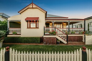 Stunning two-story home with a gabled roof and central entrance, surrounded by a white picket fence and well-maintained hedges.