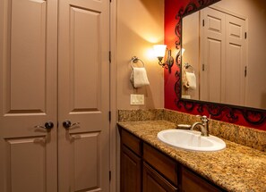 A bathroom with a white sink, granite countertop, wooden cabinets, a red accent wall, and a mirror with a black frame. - Great condo for exploring Tubac & surroundings! (Tubac)