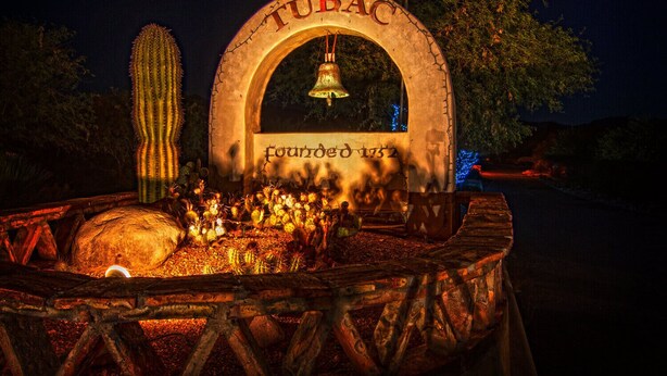 Ein historisches Denkmal mit der Aufschrift 'TUBAC Gegründet 1832' und einer Glocke, die an einem Steinbogen hängt.