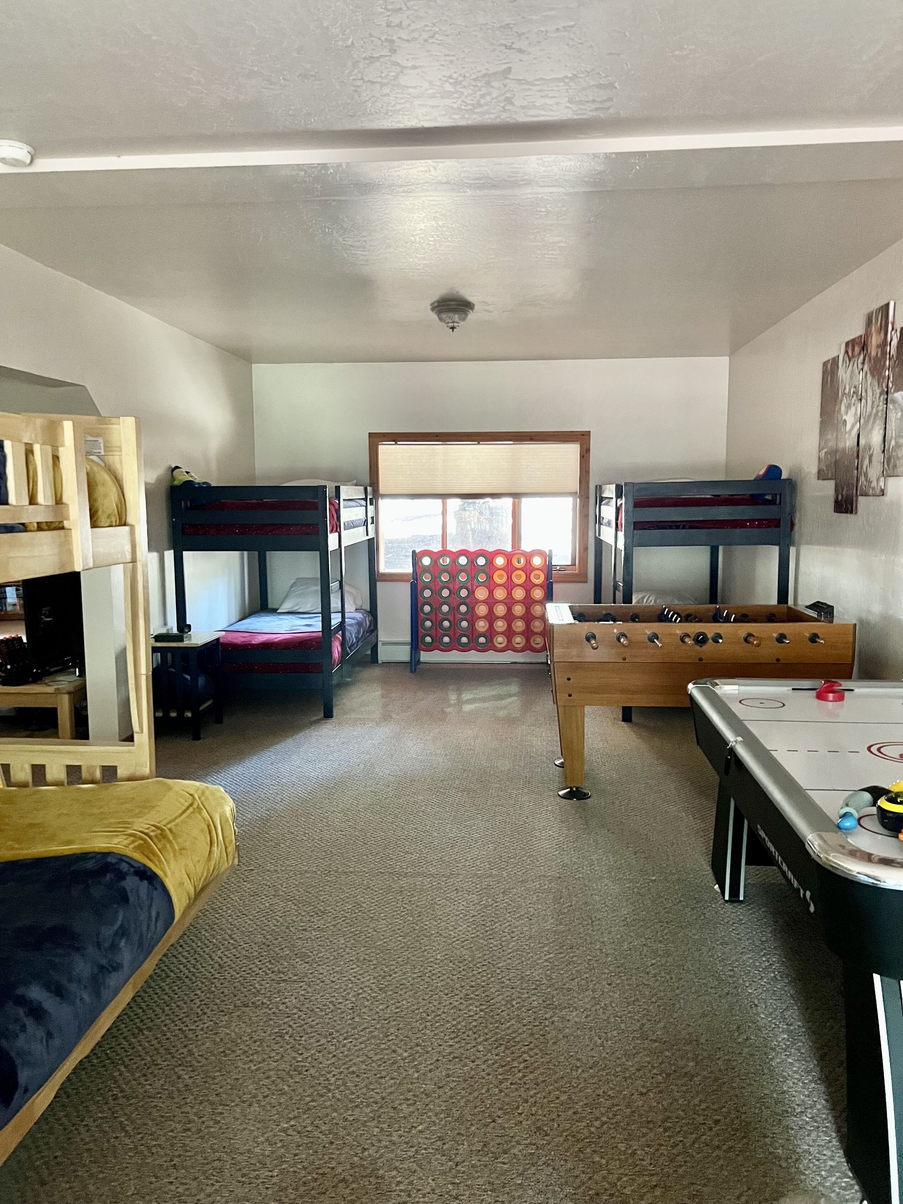 A room with bunk beds, a foosball table, and a window with blinds.