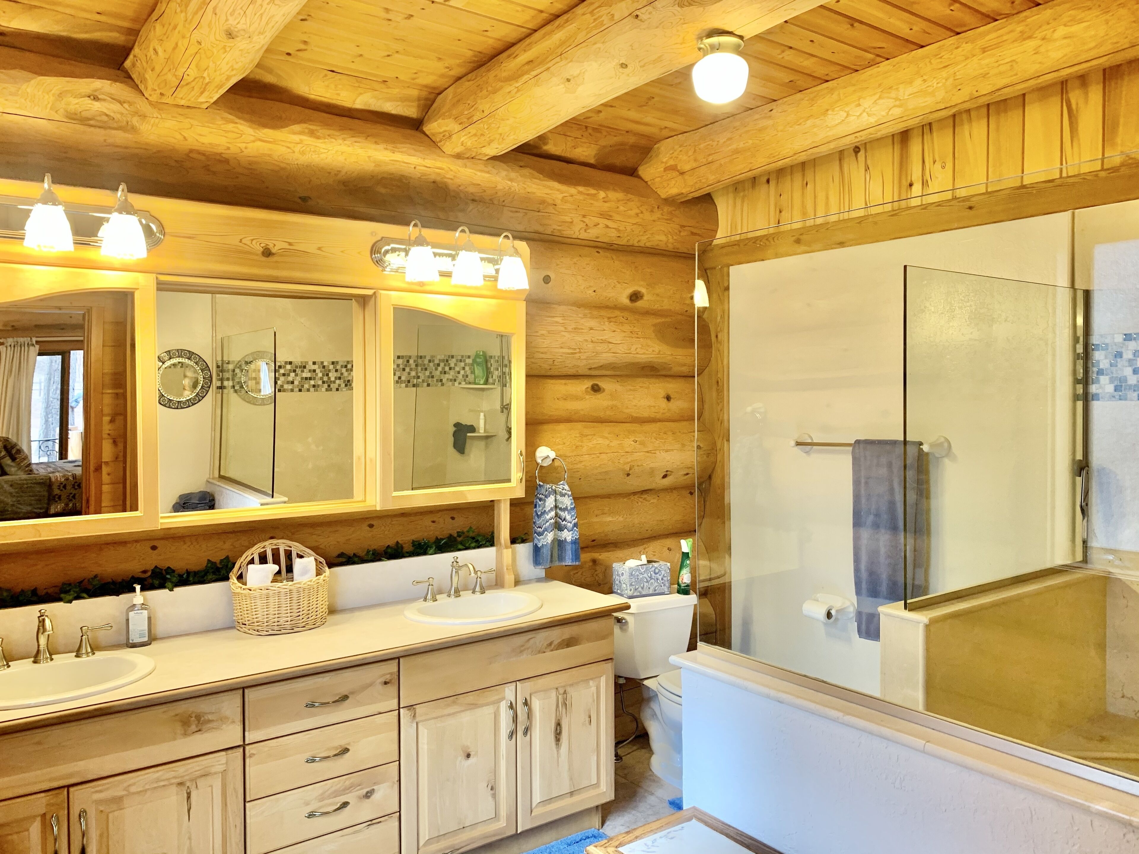 Een houten badkamer met een ruime spiegel, twee wasbakken, een douche en een houten plafond.