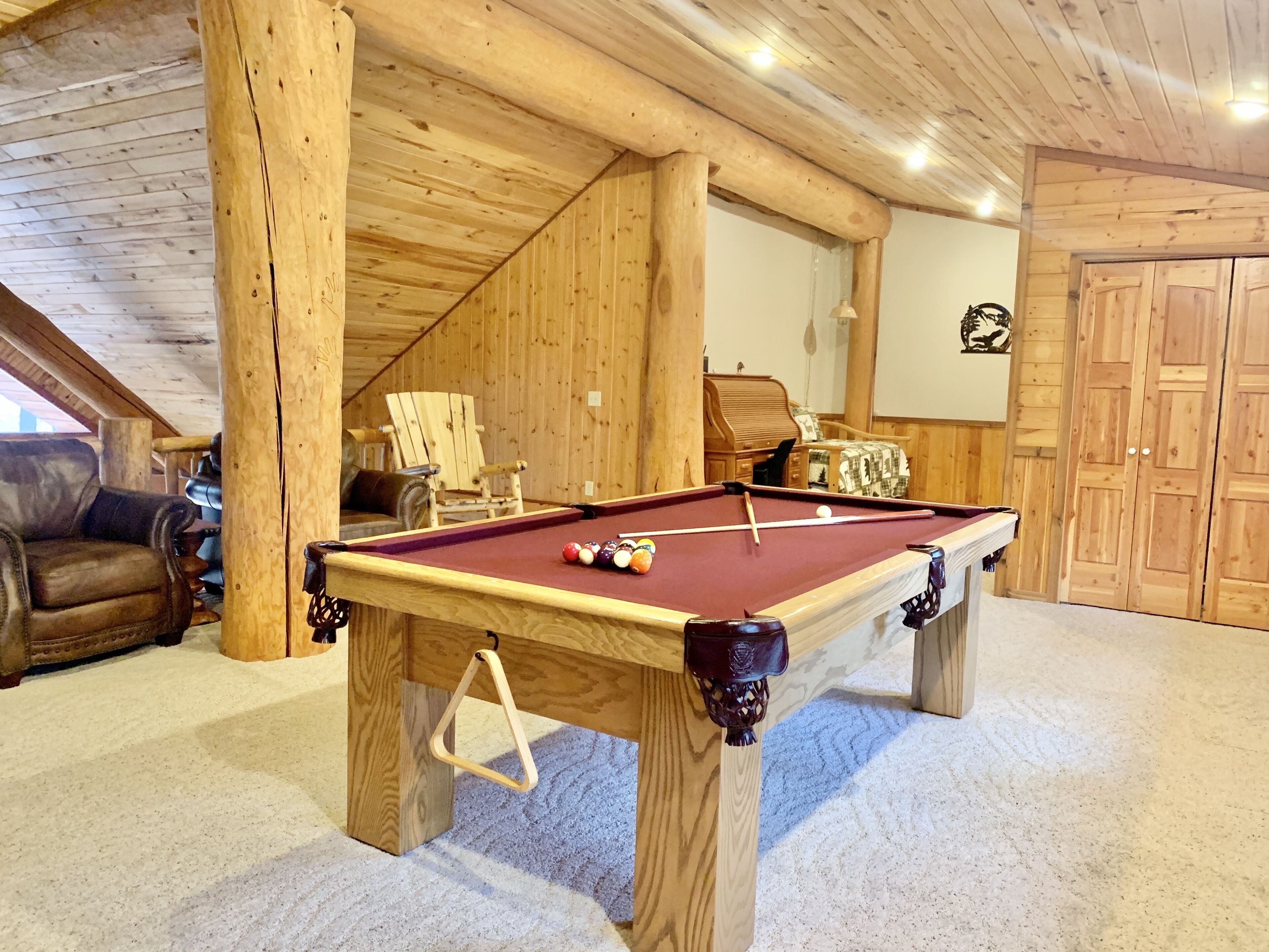 Une table de billard dans une pièce en bois, dotée d’un plafond haut et d’un coin salon confortable.