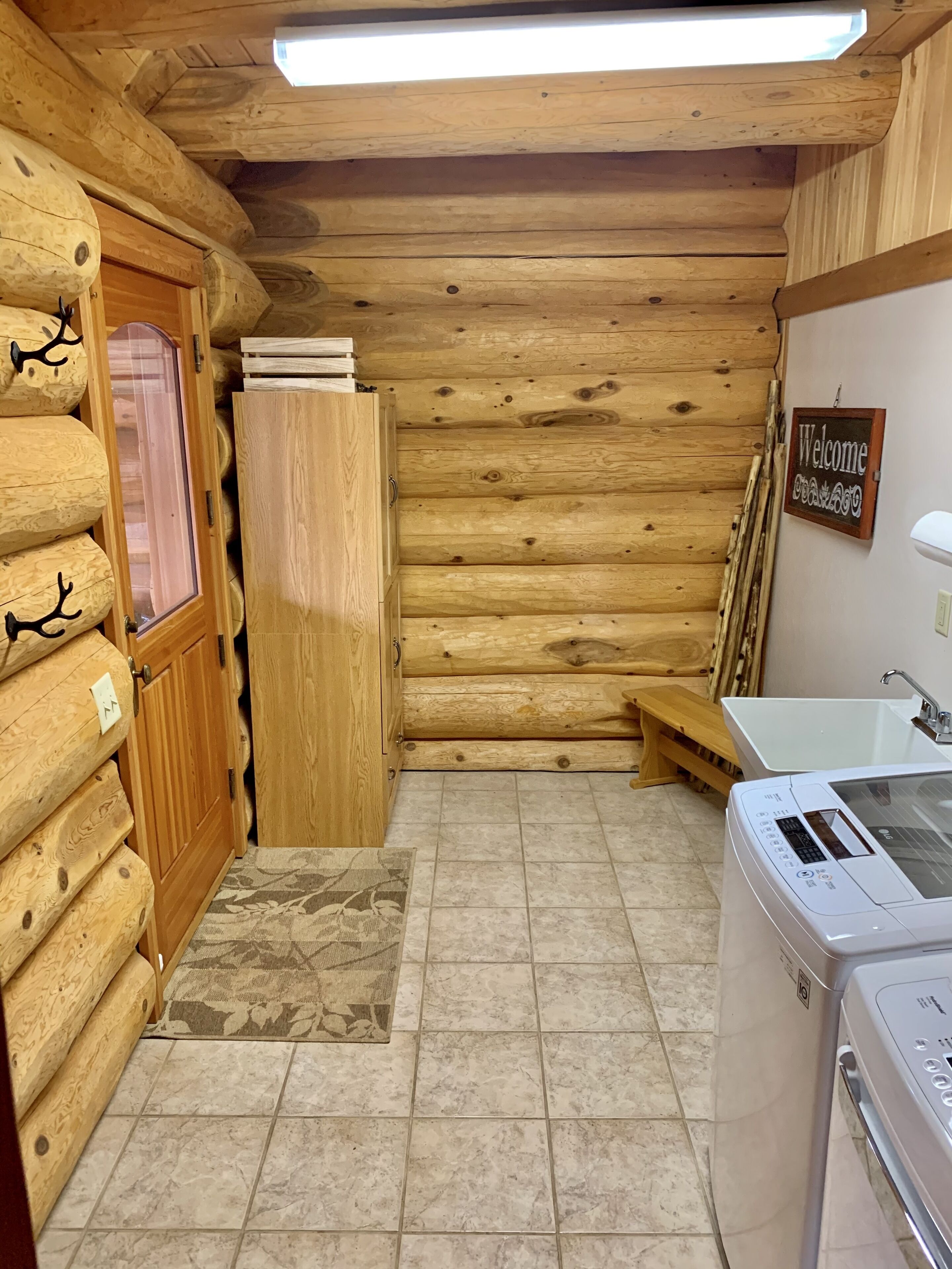 Ein rustikales Blockhaus-Interieur mit Waschmaschine, einer Bank und einem Willkommensschild.