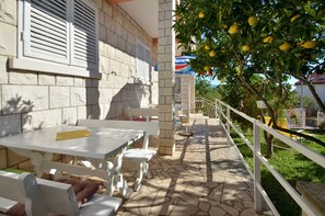 An outdoor patio area with stone flooring, white tables and benches, and a tree with lemons. - LaidBack Apartments - Standard One Bedroom Apartment with Balcony and Sea View (Orebic)