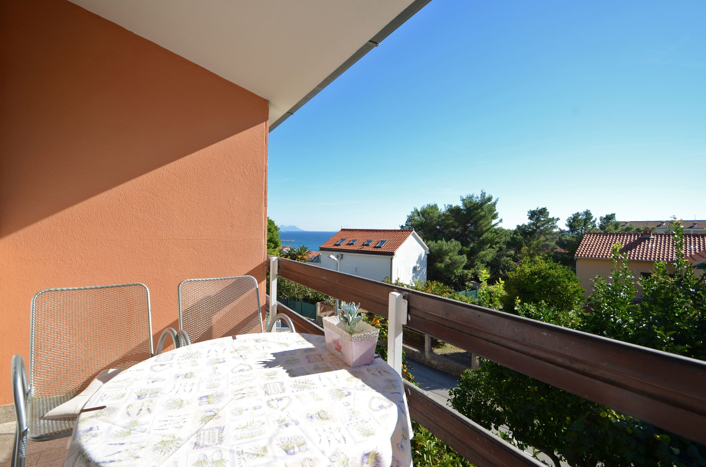 A balcony with a table and chairs, a potted plant, and a view of houses and trees.
