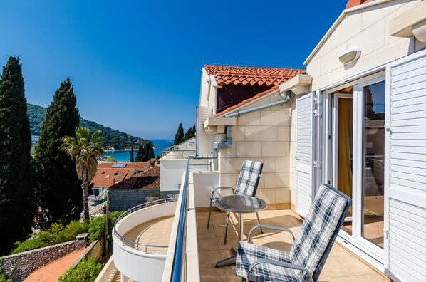 A balcony with a table and chairs, a view of the sea, and a building with a tiled roof.