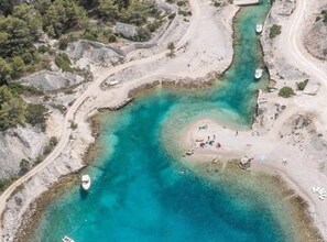An aerial view of a coastal area with clear turquoise waters, a sandy beach, and a few boats.