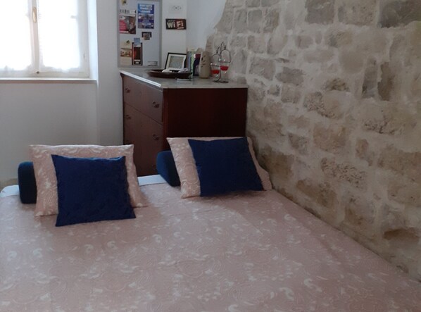 A bedroom with a bed, two pillows, a dresser, a window, and a stone wall.