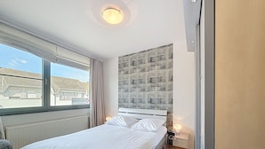 Une chambre d’hôtel avec un lit, une fenêtre, une tête de lit et une table de chevet avec une lampe.