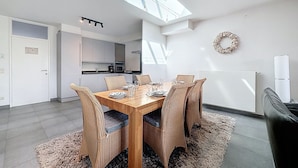 Une cuisine moderne avec des meubles blancs, une table à manger entourée de chaises en osier et une lucarne au-dessus.