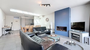 Un salon moderne avec un canapé, une table basse, une cheminée, un téléviseur et, au fond, un coin repas.