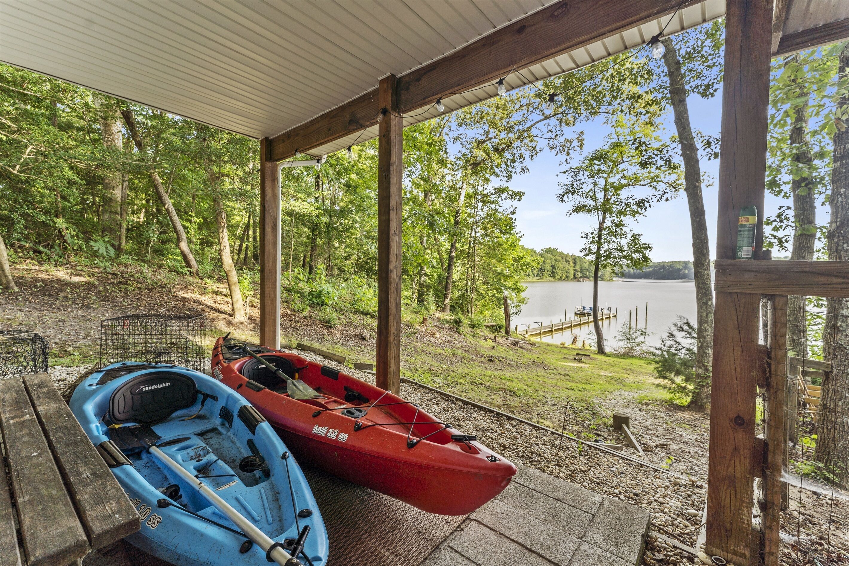 A covered outdoor area with two kayaks, a wooden bench, and a view of a lake.