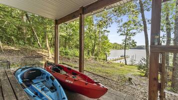 A covered outdoor area with two kayaks, a wooden bench, and a view of a lake.