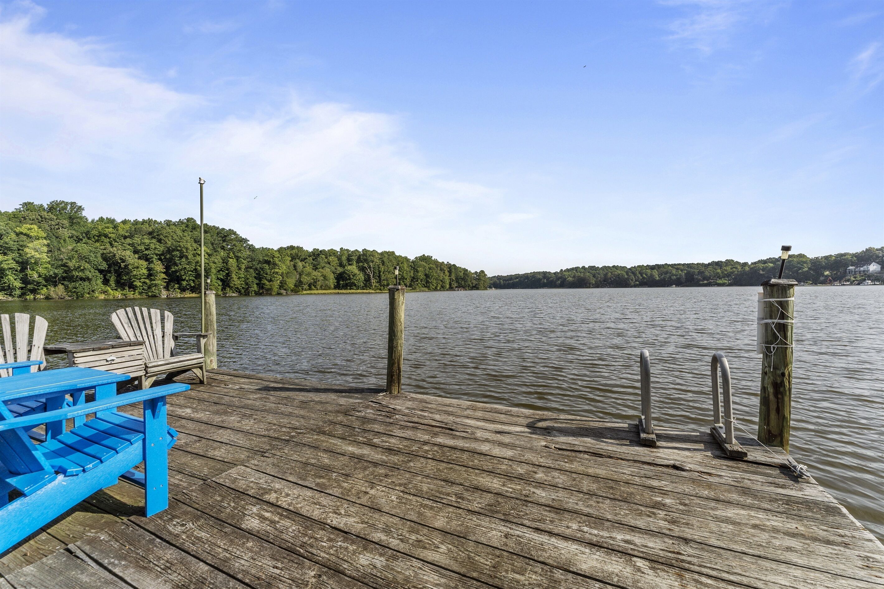 Une jetée en bois avec une chaise Adirondack bleue et deux chaises Adirondack blanches.