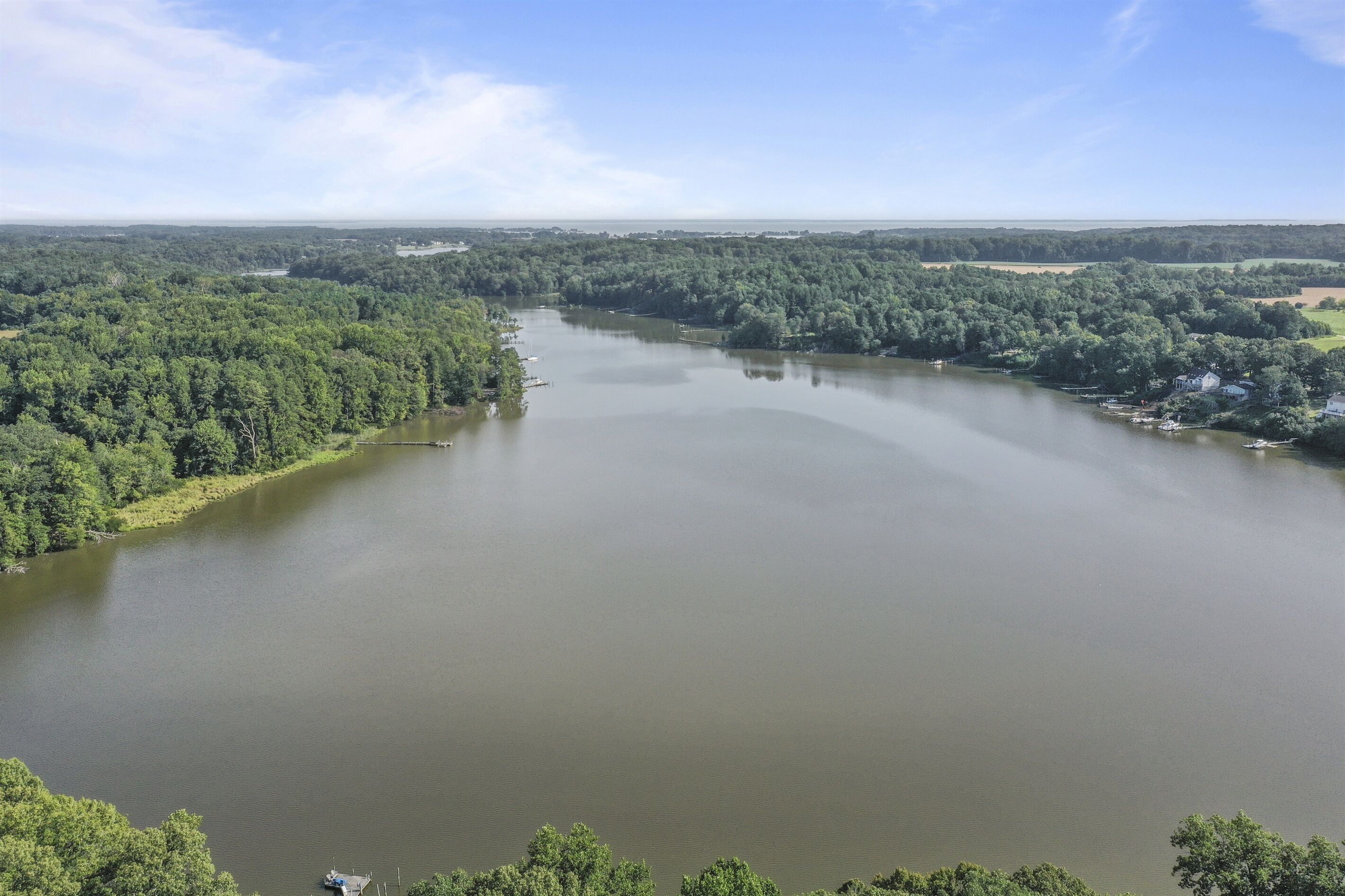 A large body of water surrounded by dense forest and a few buildings.