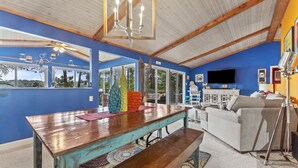 A spacious room with a wooden dining table, a bench, a sofa, and a television. - Waterfront 3BR/3BA Getaway: Beach, Dock, Firepit! AMAZING Sweeping VIEWS! (Heathsville)