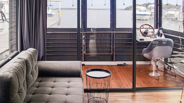 Ein modernes Interieur mit einer Couch, einem runden Tisch und Blick auf eine Marina durch große Fenster.