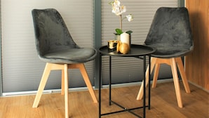 Zwei dunkelgraue Polsterstühle mit Holzbeinen, ein runder Tisch mit schwarzem Metallgestell und eine Orchidee im Topf auf dem Tisch.