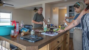 A kitchen counter with various food items and a person preparing food. - Sunset Views over Rachel Carson Preserve. Relax steps from Wells Beach. (Wells)