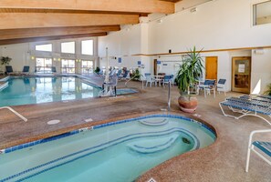 An indoor swimming pool with multiple lanes, lounge chairs, and a large potted plant.