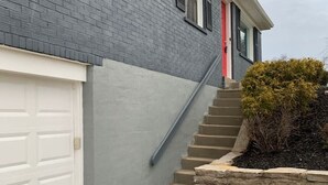 Un edificio residencial con garaje, una puerta roja y una escalera que lleva a la entrada.