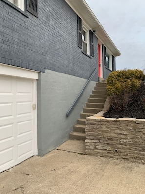 A residential building with a garage, a red door, and a staircase leading to the entrance.