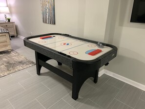 A pool table with a light-colored playing surface and dark edges, positioned in a room with light gray flooring and a small rug.